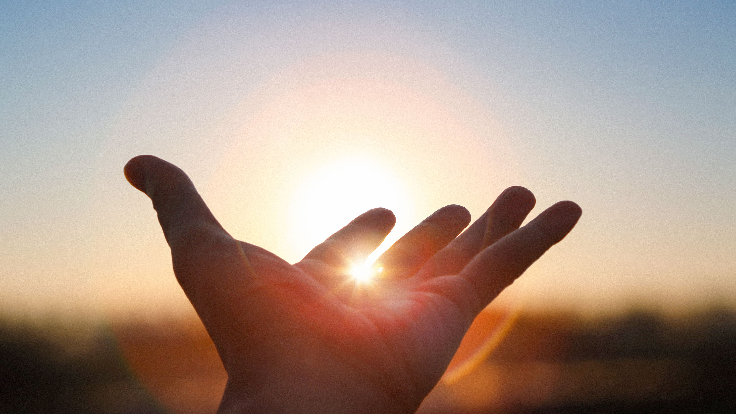 Hands stretched out with the rising sun showing between two fingers