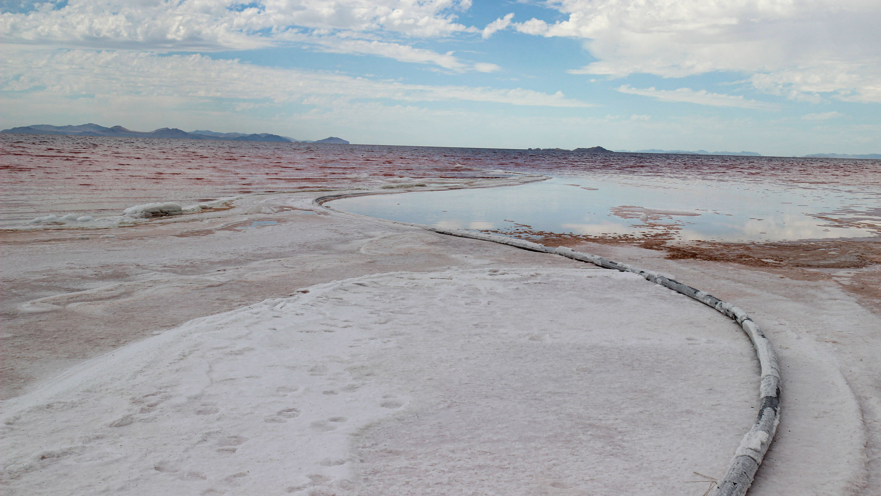 a black hose crusted and partly buried with white and pink minerals winds into a pool of water