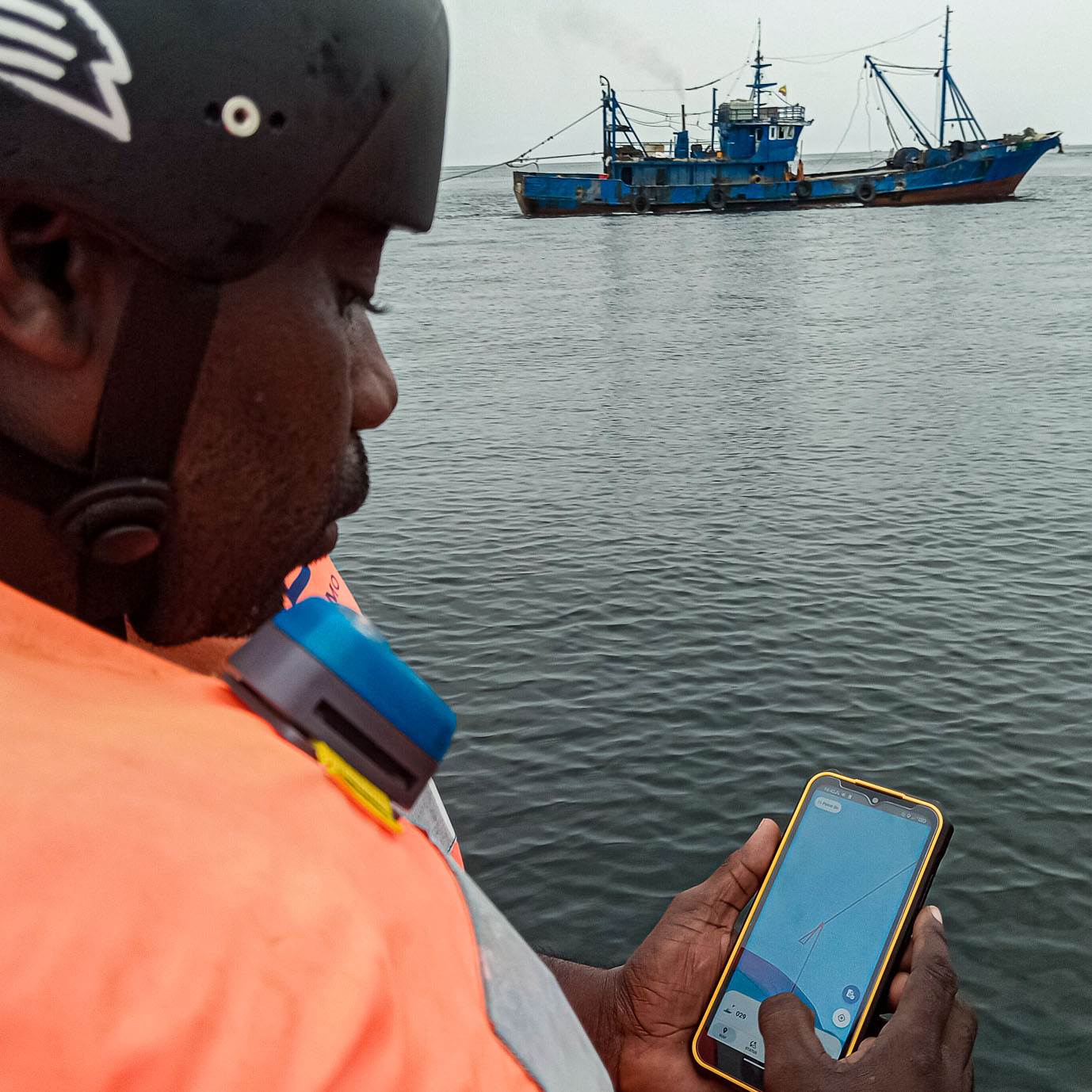 person holds a phone with the app while looking at a nearby vessel at sea