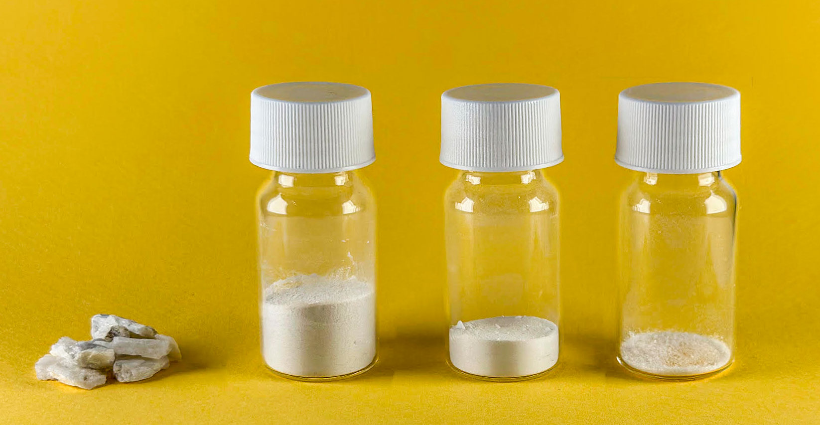 small pieces of rock next to a line of 3 capped vials of powder